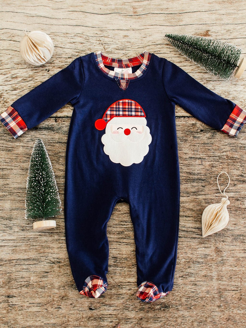 navy long sleeve infant boys romper flay lay showing a santa wearing a red, navy, and white plaid hat applique in center and same plaid details at collor, trim of sleeves, and footies 