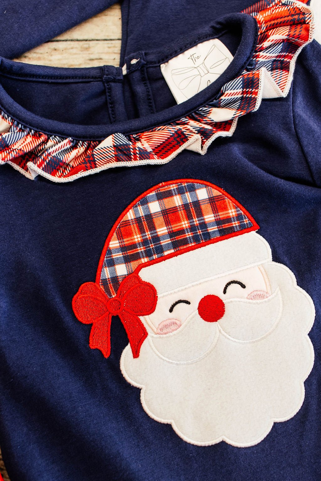 close up of the santa applique showing the red navy and white plaid hat on santa and the plaid ruffle collar