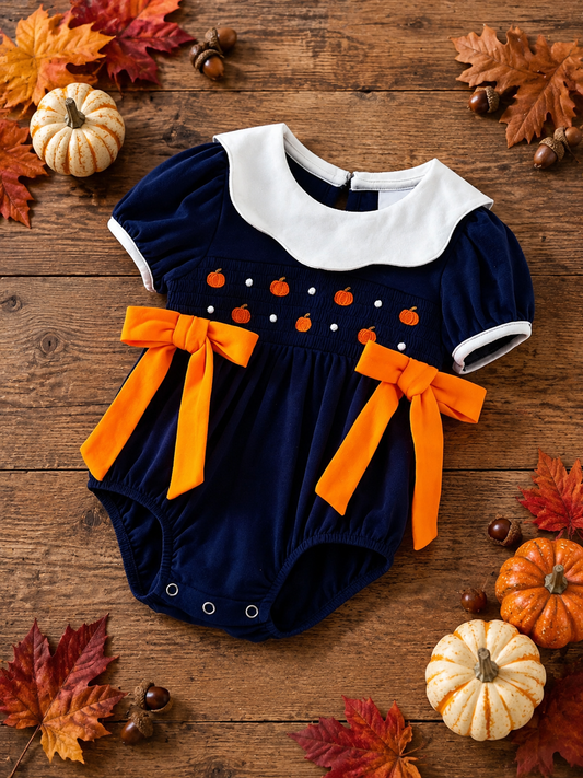 Navy girls fall dress with pumpkin smocking on a rustic autumn background.
