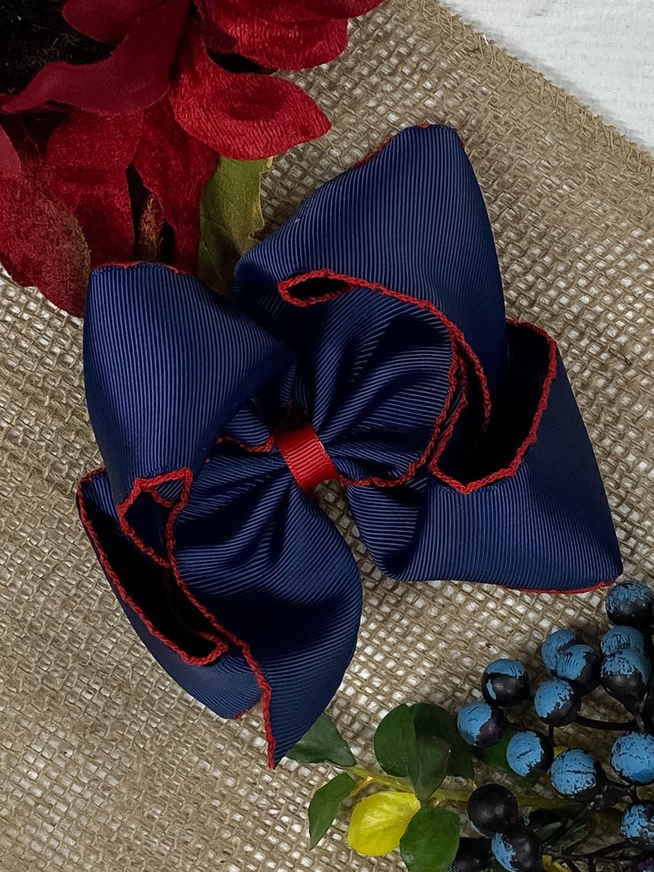 A navy blue hair bow with red moonstitch detailing on a burlap background.