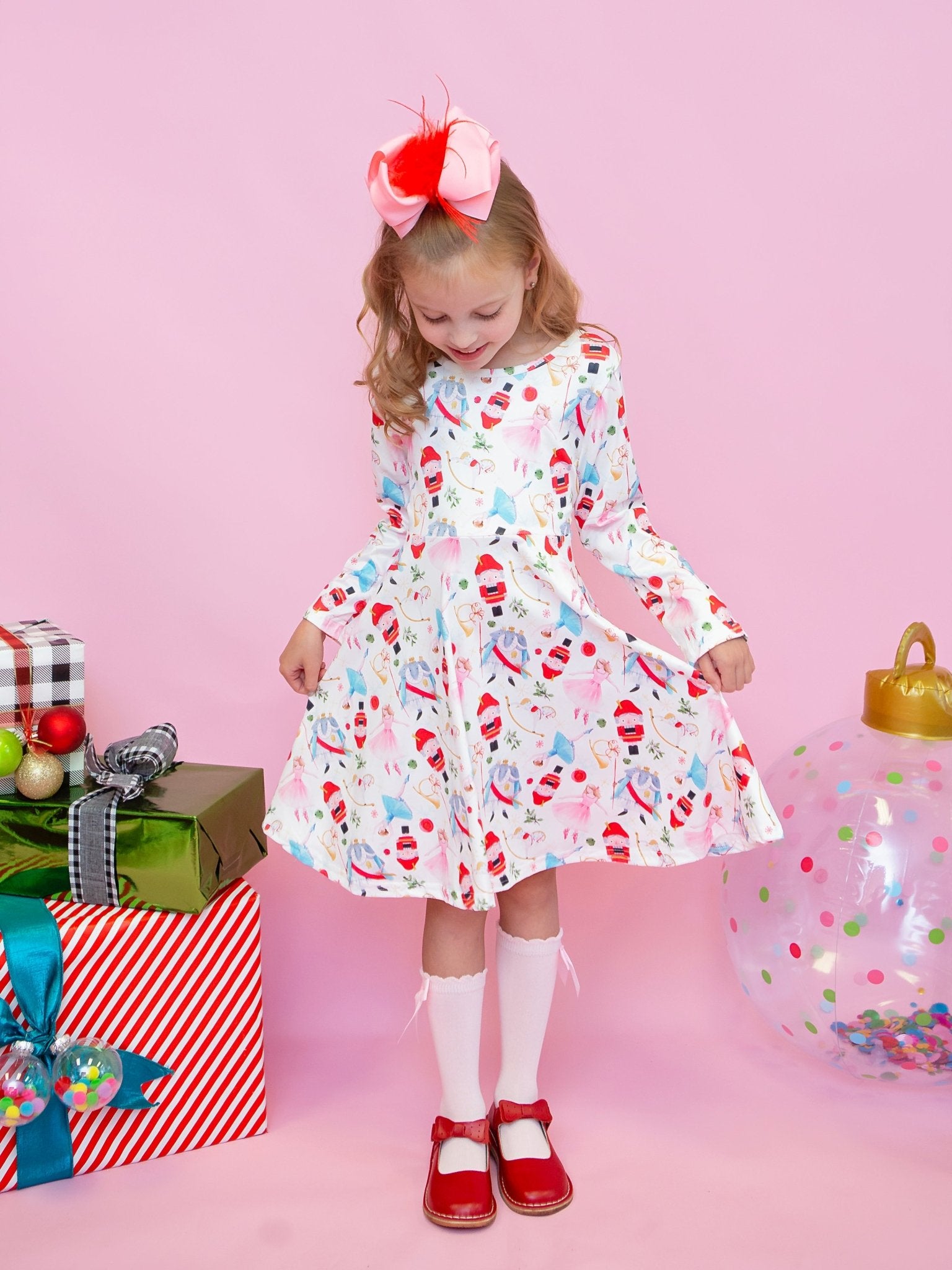 Young girl in a patterned dress with Christmas-themed decorations on a pink background