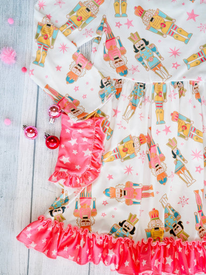 Close-up of the Nutcracker Galore Twirl Dress with Pockets, featuring a colorful nutcracker print on white fabric with pink star accents. The dress includes pink star-patterned side pockets with ruffled trim and a coordinating ruffle hem along the skirt.