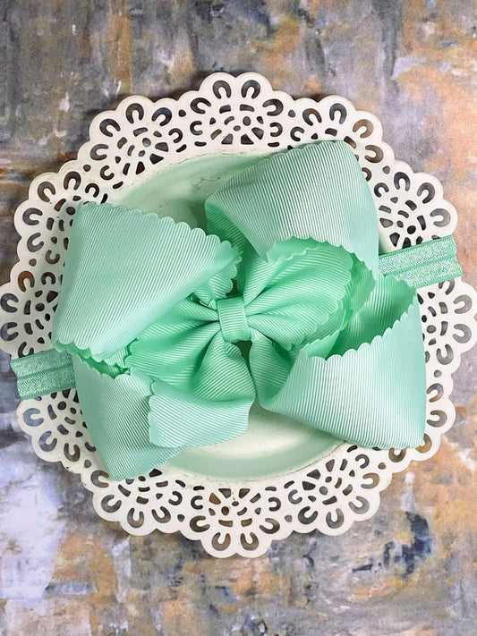Mint green bow hair clip on a decorative white base against a textured background