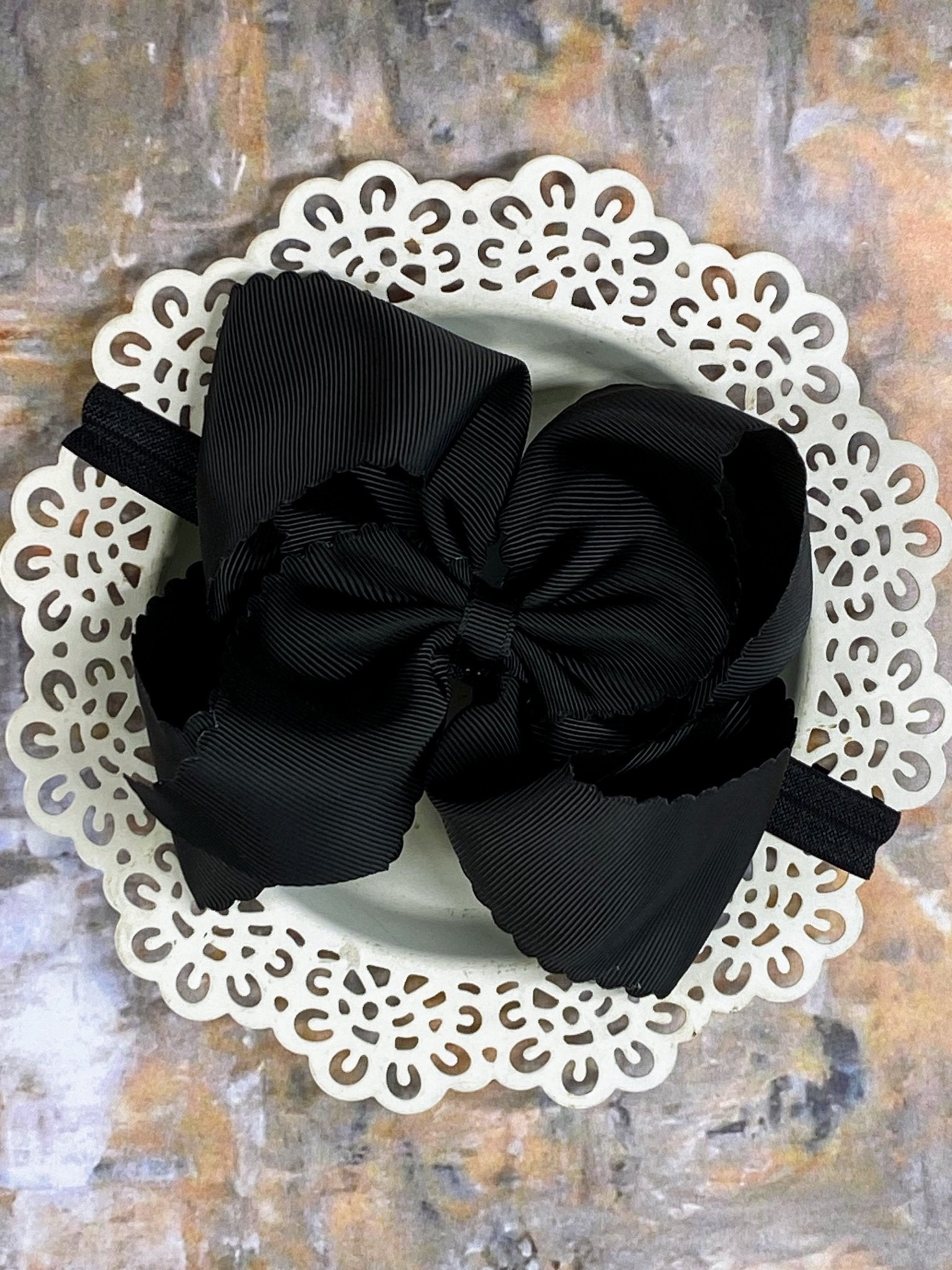Black hair bow  headband on a white doily with a textured background