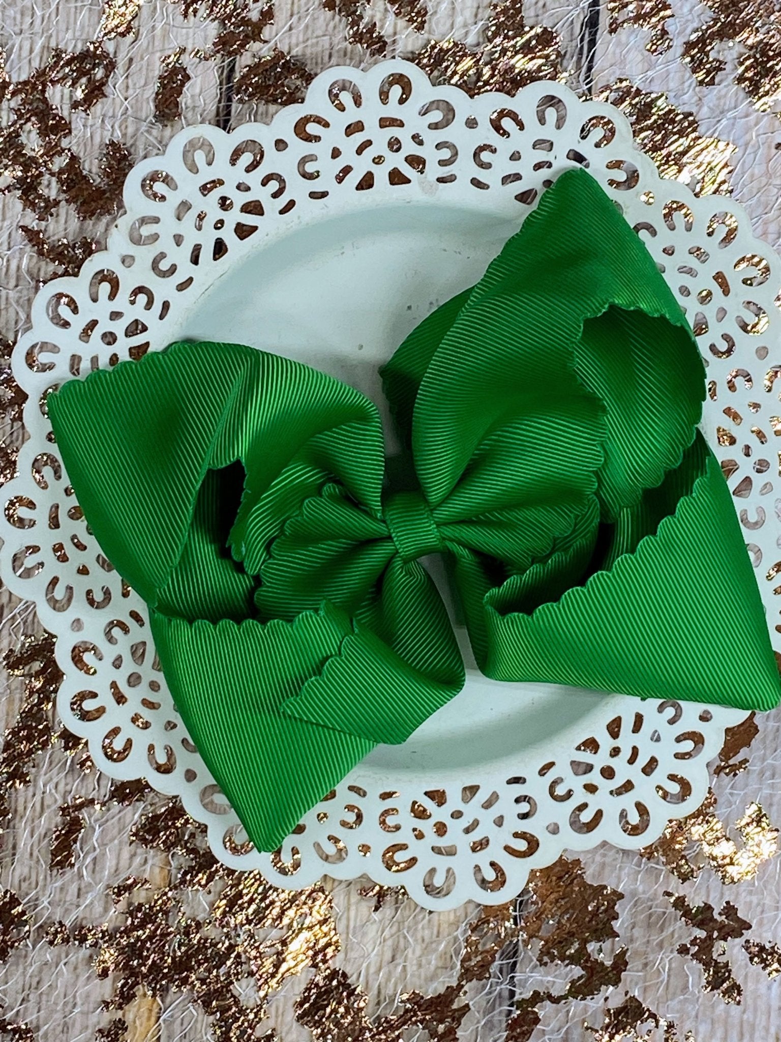 Green hair bow on a white doily with a gold leaf background