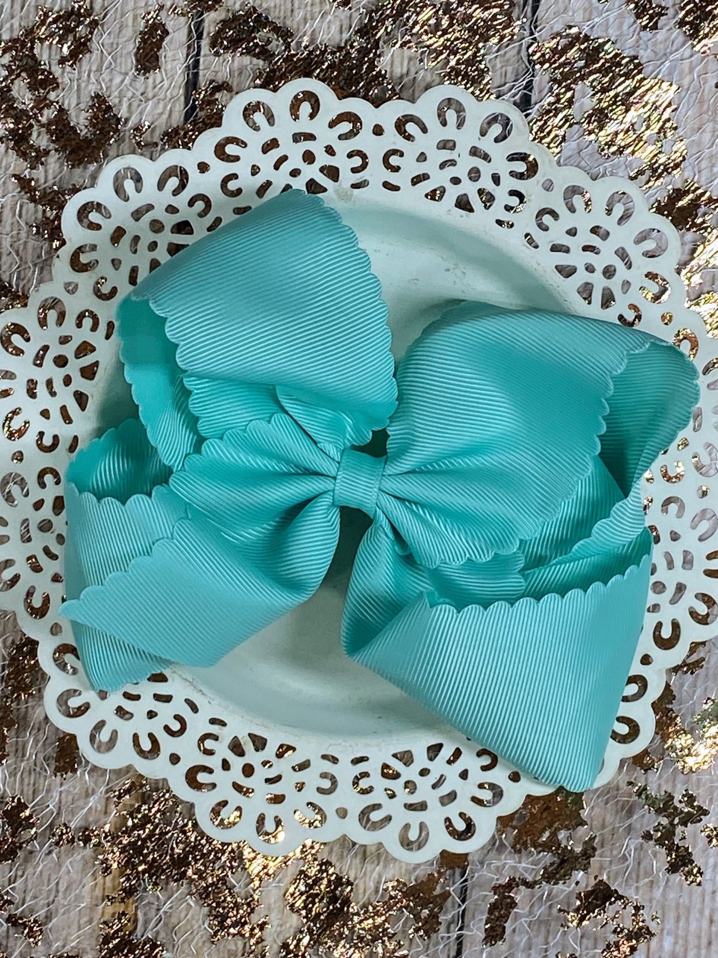 Two turquoise bows on a white lace doily with a gold and brown patterned background.