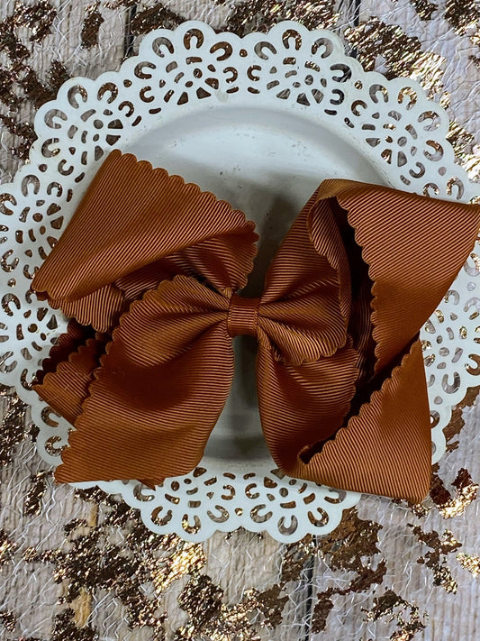 scalloped brown hair bow on a decorative white plate with a gold glittery background
