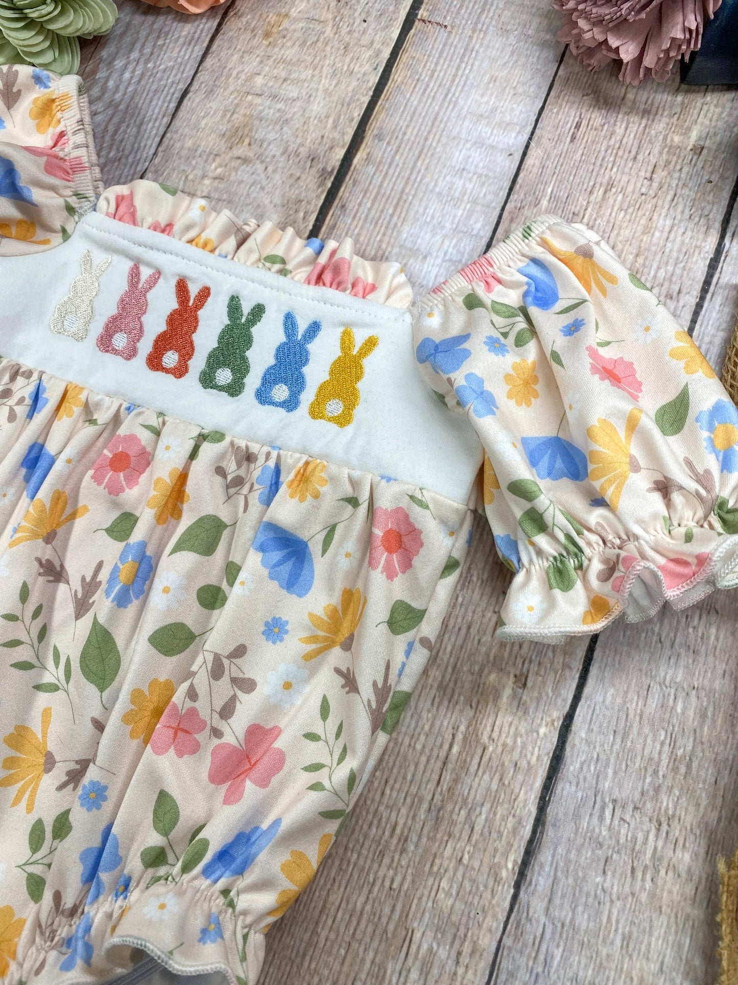 Children's outfit with floral pattern and embroidered bunnies on a wooden surface