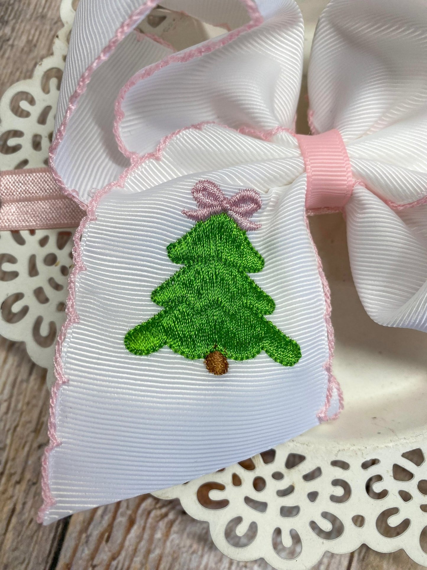 White ribbon bow with green embroidered Christmas tree and pink bow on decorative background