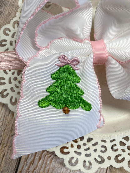White ribbon bow with green embroidered Christmas tree and pink bow on decorative background