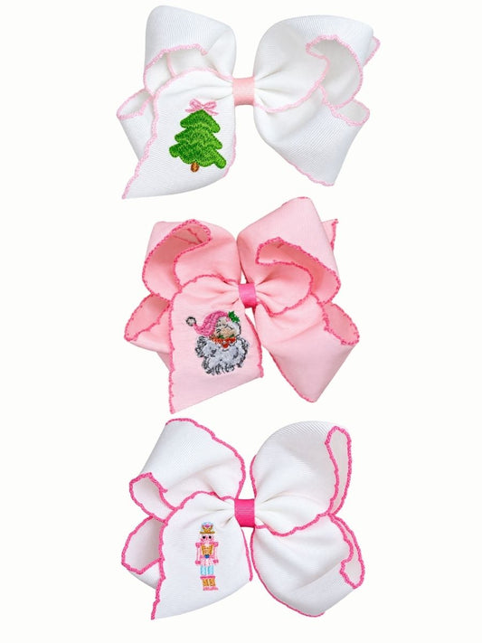 Three pink embroidered Christmas hair bows stacked on a white background: a pink Santa bow, a pink nutcracker bow and a pink Christmas tree bow