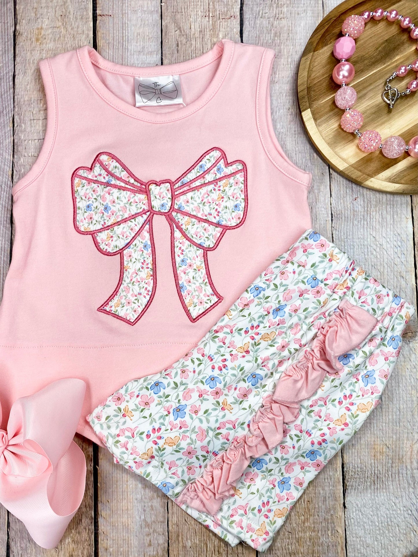 Pink sleeveless top with a large bow and matching floral shorts on wooden background