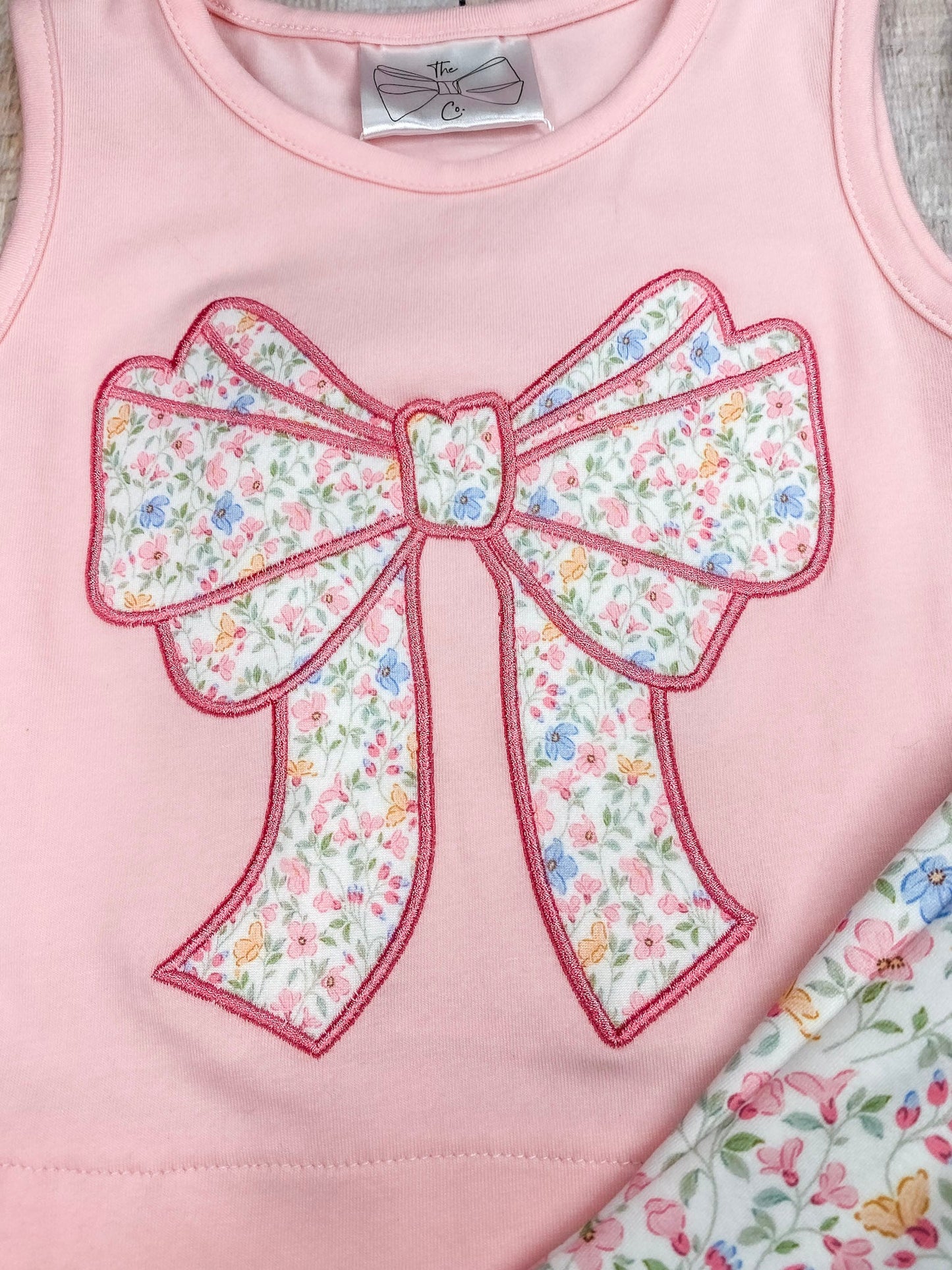 Pink sleeveless top with a large bow and matching floral shorts on wooden background