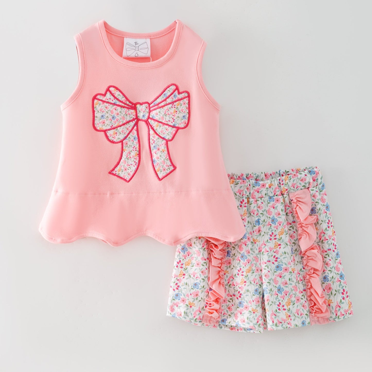 Pink sleeveless top with a large bow and matching floral shorts on a light gray background