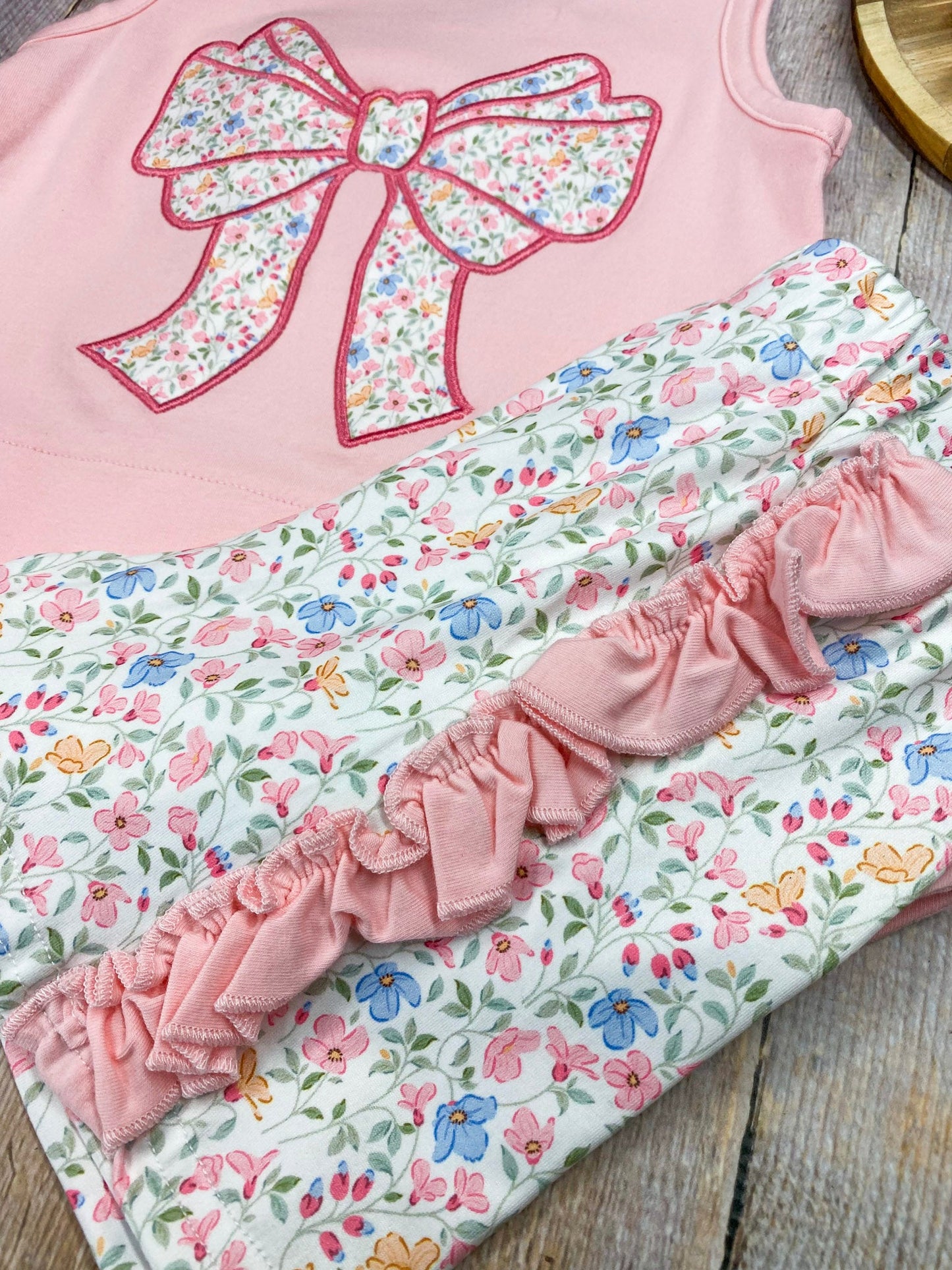 Pink sleeveless top with a large bow and matching floral shorts on wooden background
