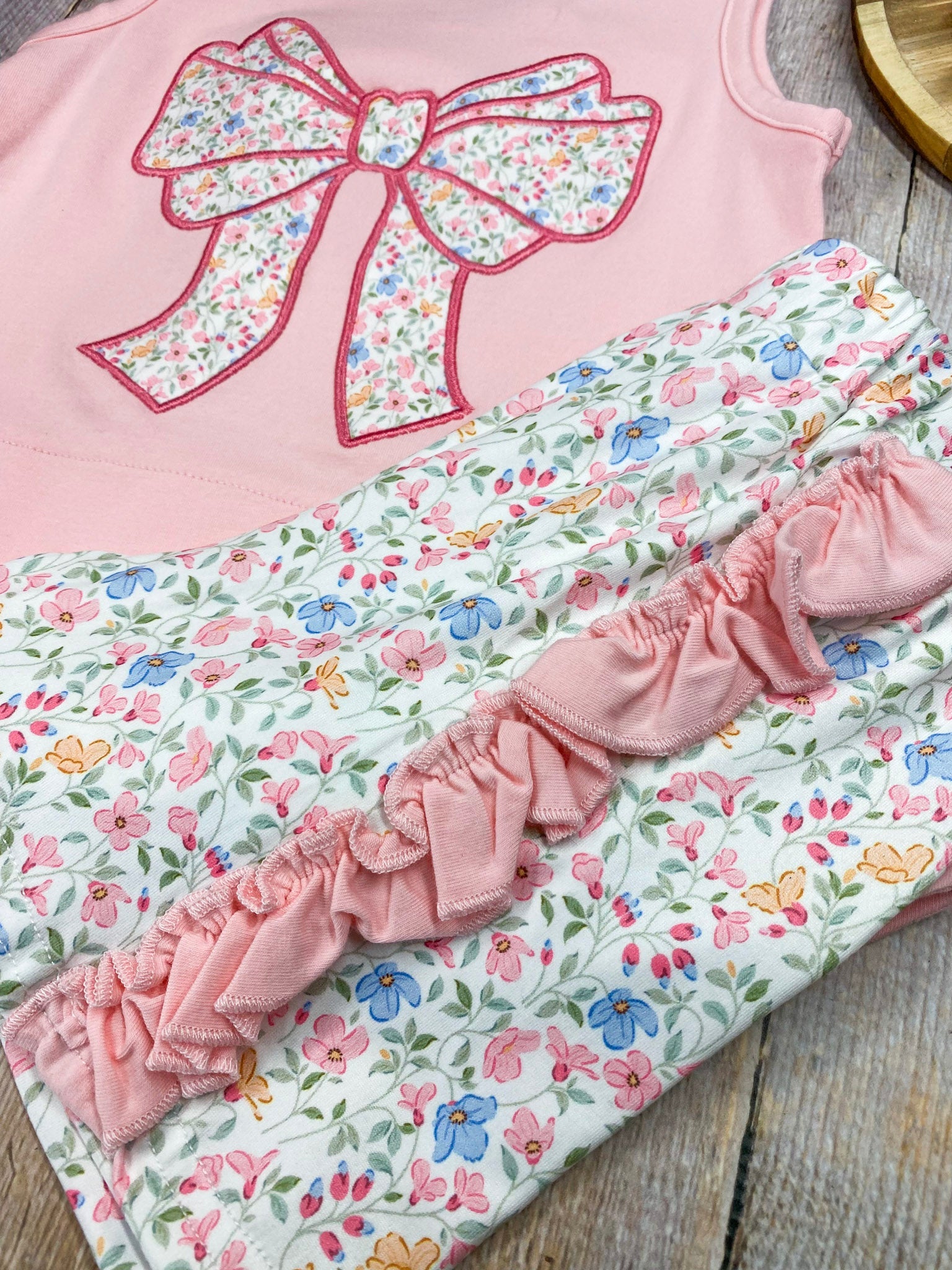 Pink sleeveless top with a large bow and matching floral shorts on wooden background