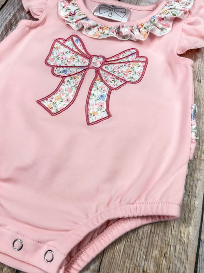 Pink baby romper with floral bow and ruffles on a wooden background
