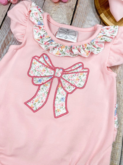 Pink baby romper with floral bow and ruffles on a wooden background