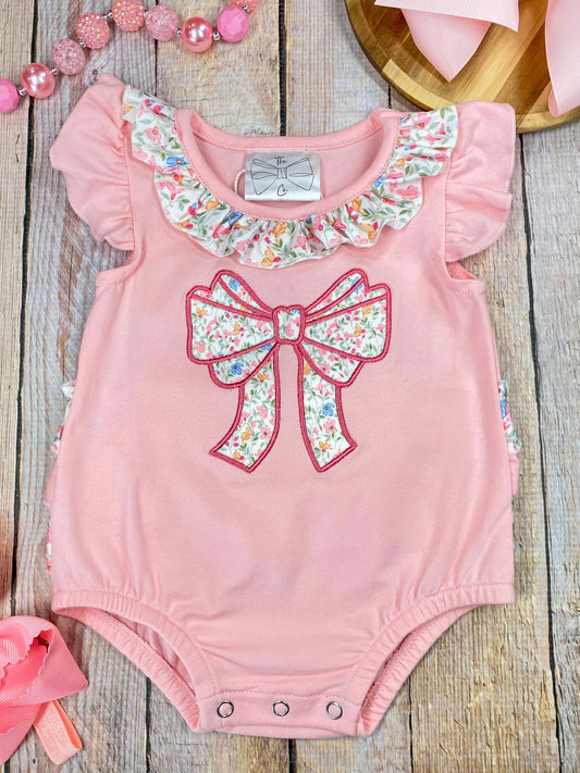Pink baby romper with floral bow and ruffles on a wooden background