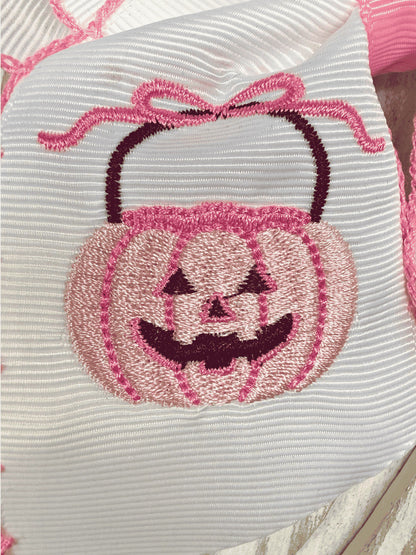 Close-up of embroidered pink jack-o'-lantern on white hair bow
