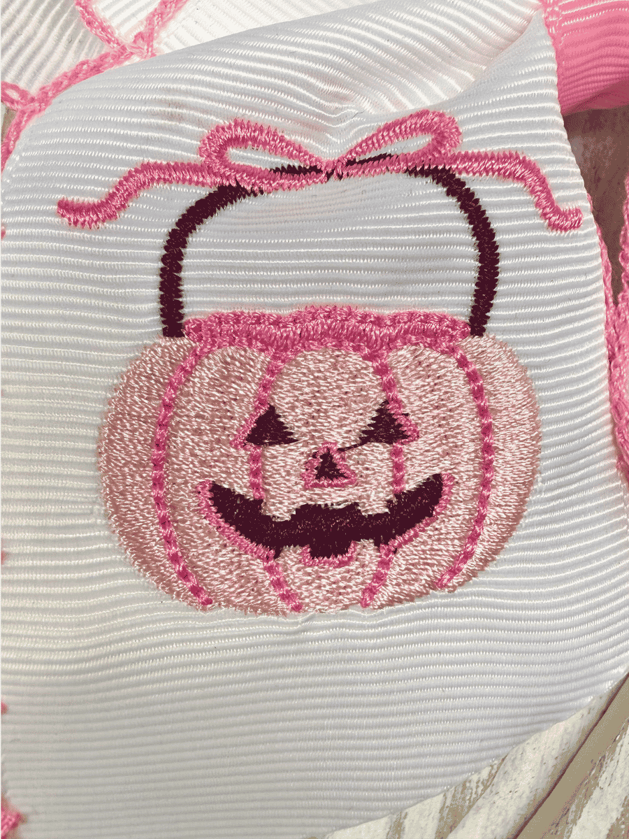 Close-up of embroidered pink jack-o'-lantern on white hair bow