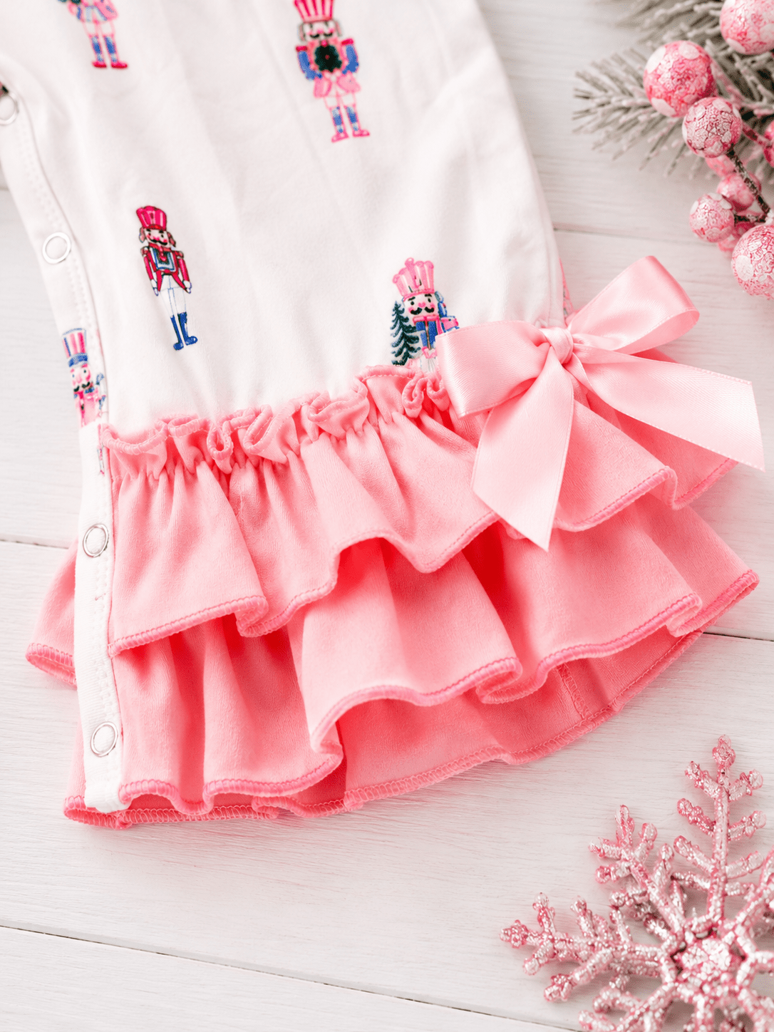 Close-up of Pink Nutcracker Christmas infant romper with pastel nutcracker print, layered ruffle legs, and pink bow detail.