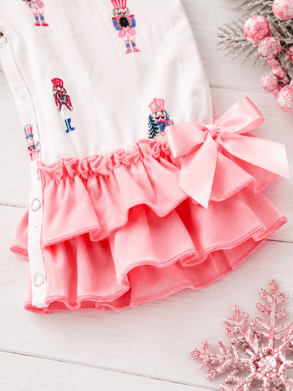 Close-up of Pink Nutcracker Christmas infant romper with pastel nutcracker print, layered ruffle legs, and pink bow detail.
