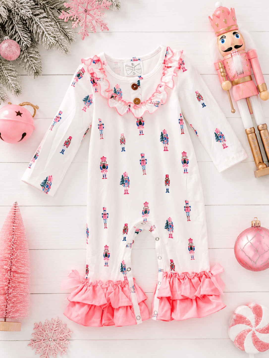 Pink Nutcracker Christmas infant romper featuring a pastel nutcracker print, ruffle trim, and festive holiday flatlay.