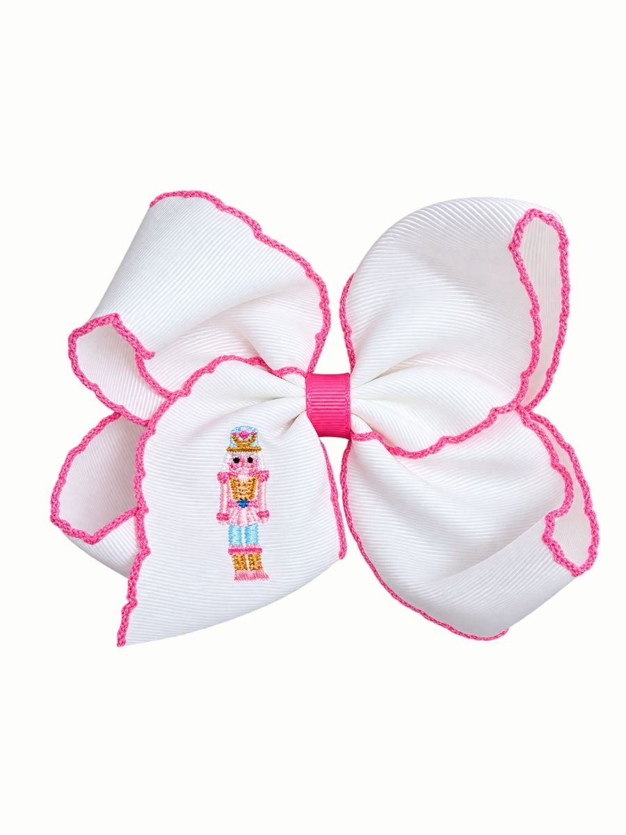 Pink moonstitch hair bow with an embroidered nutcracker soldier on the tail, on a white background