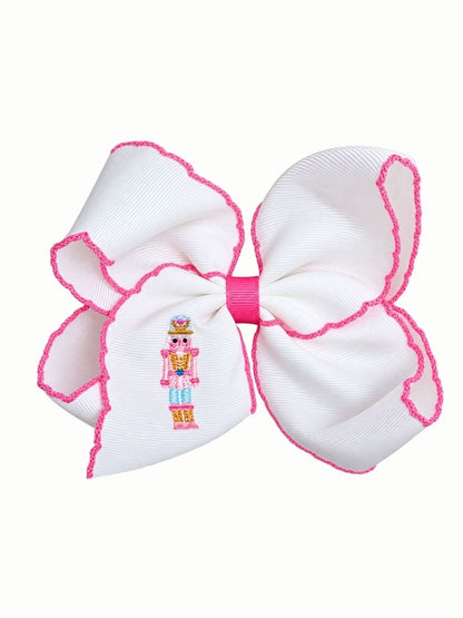 Pink moonstitch hair bow with an embroidered nutcracker soldier on the tail, on a white background