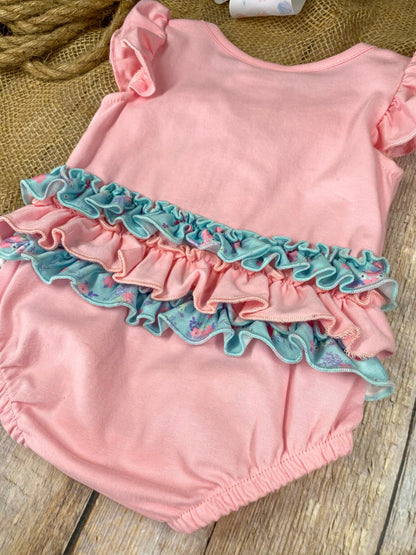 Pink baby romper with a blue bow design on a wooden background