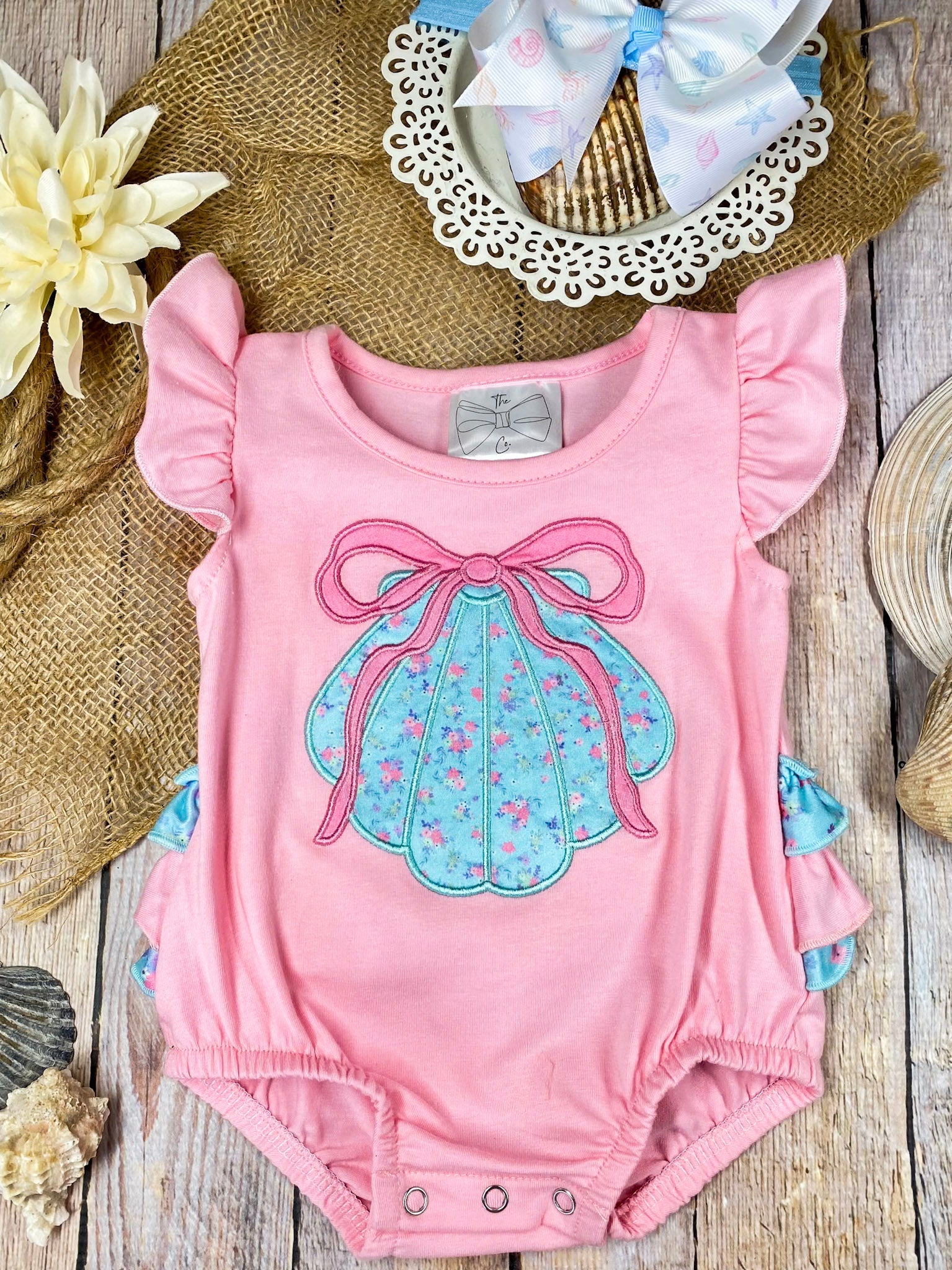 Pink baby romper with a blue bow design on a wooden background