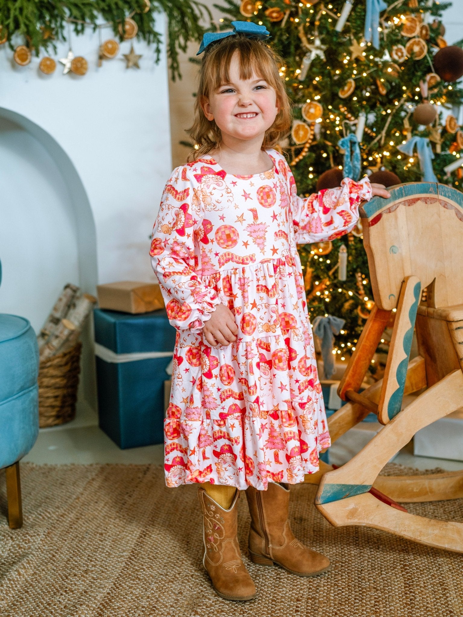 Young girl in a floral dress standing in front of a decorated Christmas tree.