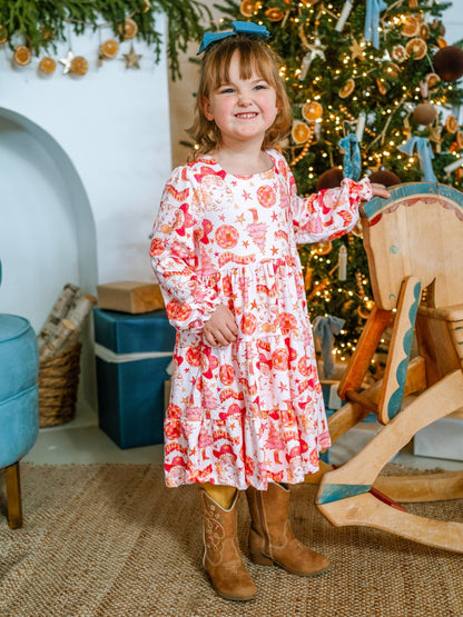 Young girl in a floral dress standing in front of a decorated Christmas tree.