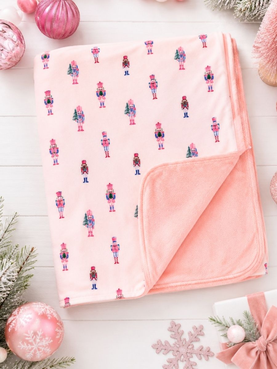 Pink Nutcracker Christmas minky baby blanket with pastel nutcracker print and ultra-soft blush plush backing in a festive holiday flatlay.