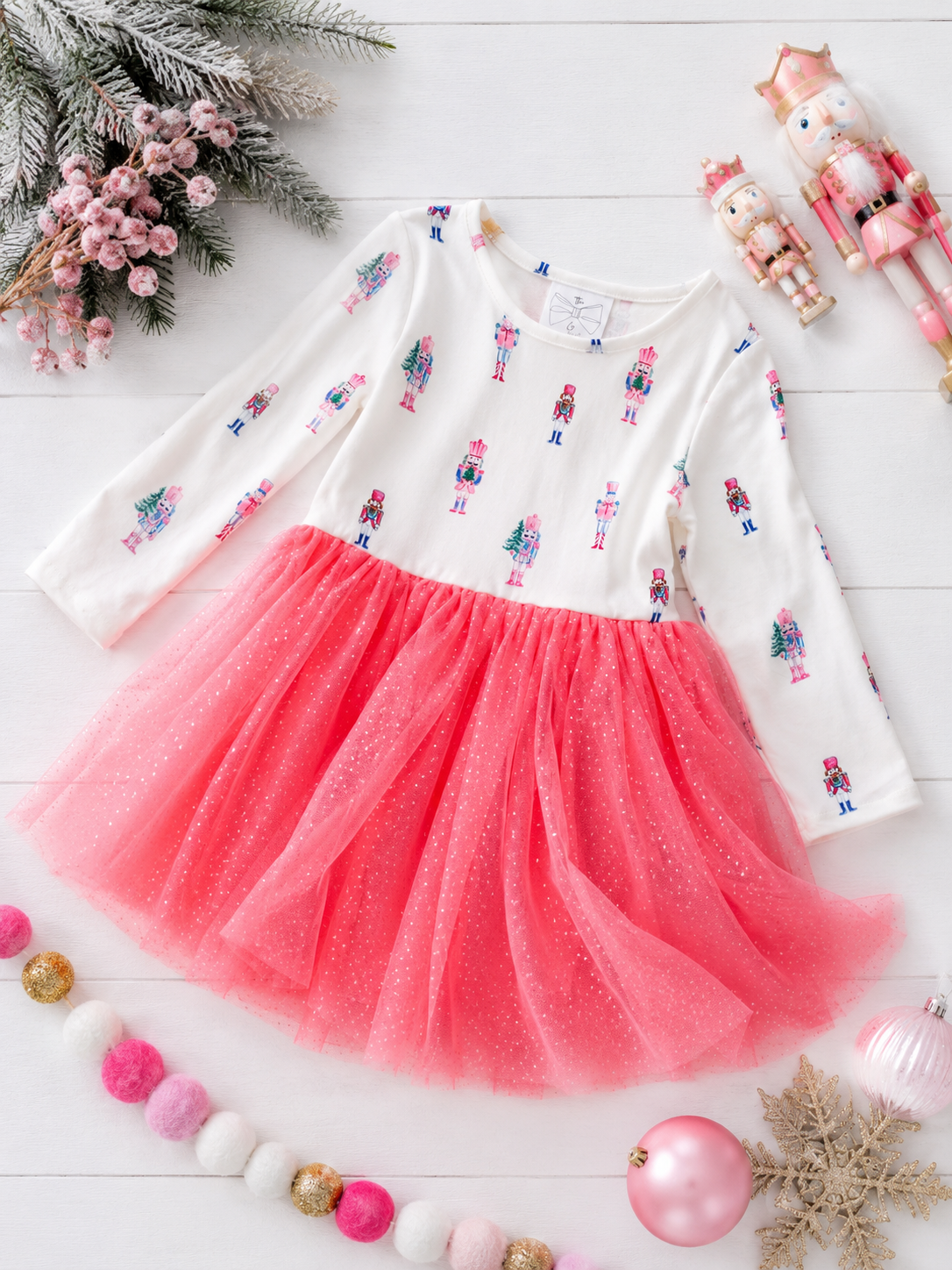 Pink Nutcracker Christmas tutu dress for girls with a pastel nutcracker print, sparkly pink tulle skirt, and long sleeves in a festive holiday flatlay.