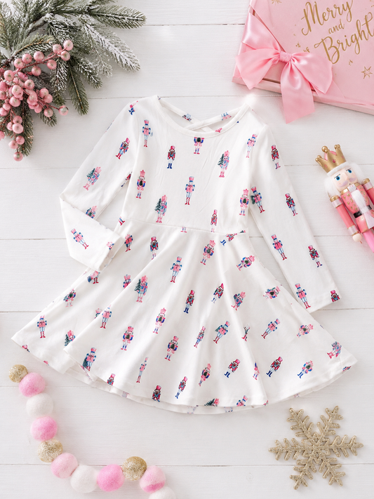 Pink Nutcracker Christmas twirl dress with pastel nutcracker print, long sleeves, and a full twirl skirt in a festive holiday flatlay.