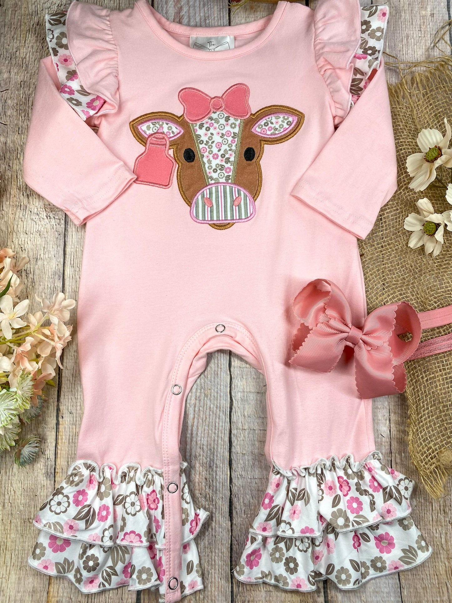 baby girl western one-piece with floral cow appliqué and layered floral ruffle leg hems on a wooden background