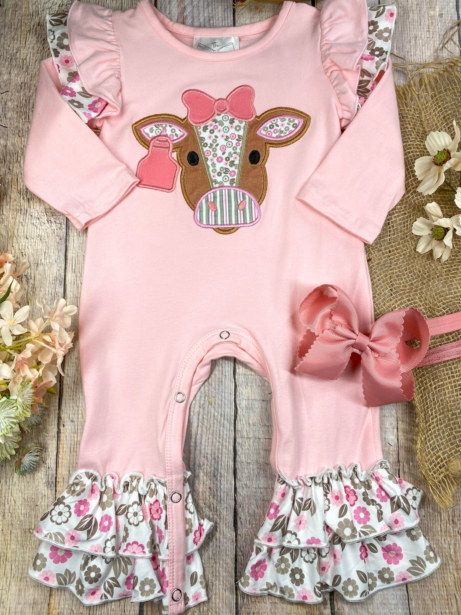 baby girl western one-piece with floral cow appliqué and layered floral ruffle leg hems on a wooden background