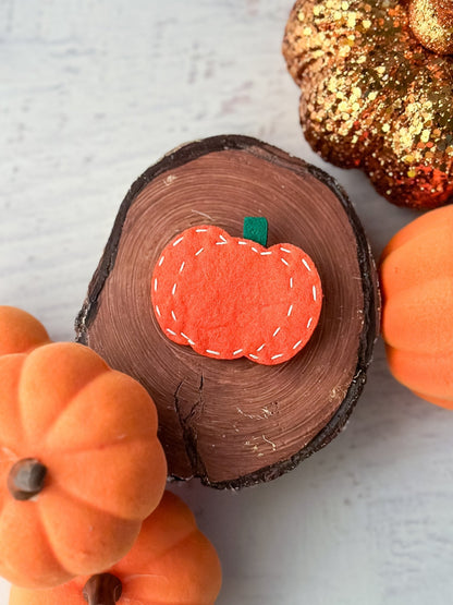 Pumpkin felt clippie displayed on a wooden log with pumpkins