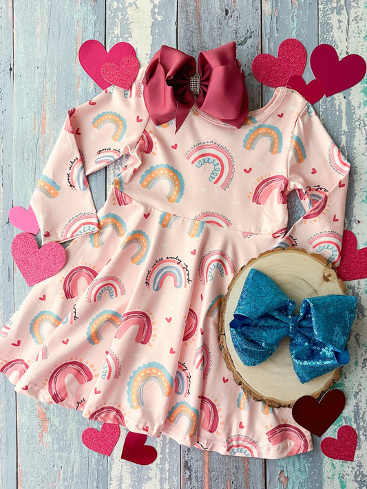 A long sleeve dress with a pink background featuring rainbow patterns and various colorful embellishments including a bow tie on the side.