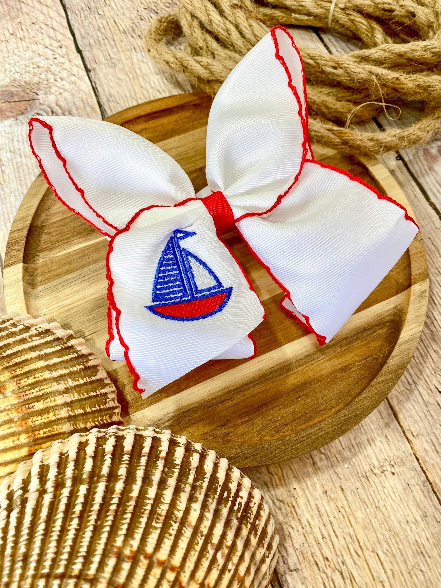 white hairbow with red trim and embroidered sailboat on a wooden surface