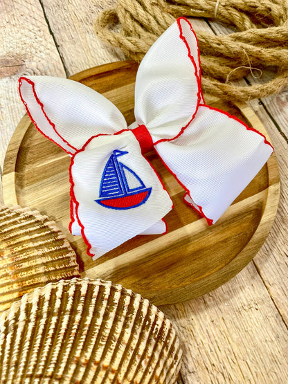 white hairbow with red trim and embroidered sailboat on a wooden surface