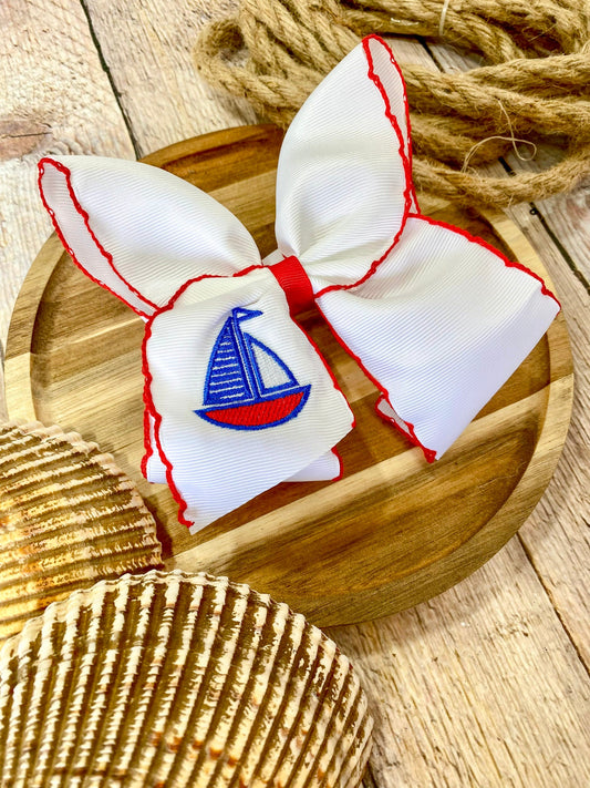 white hairbow with red trim and embroidered sailboat on a wooden surface - Alternative view