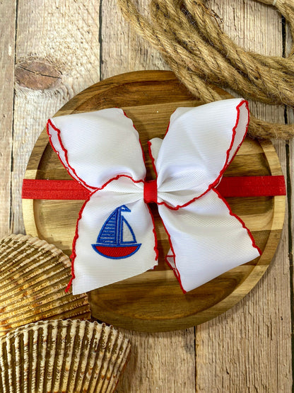 white headband with red trim and embroidered sailboat on a wooden surface