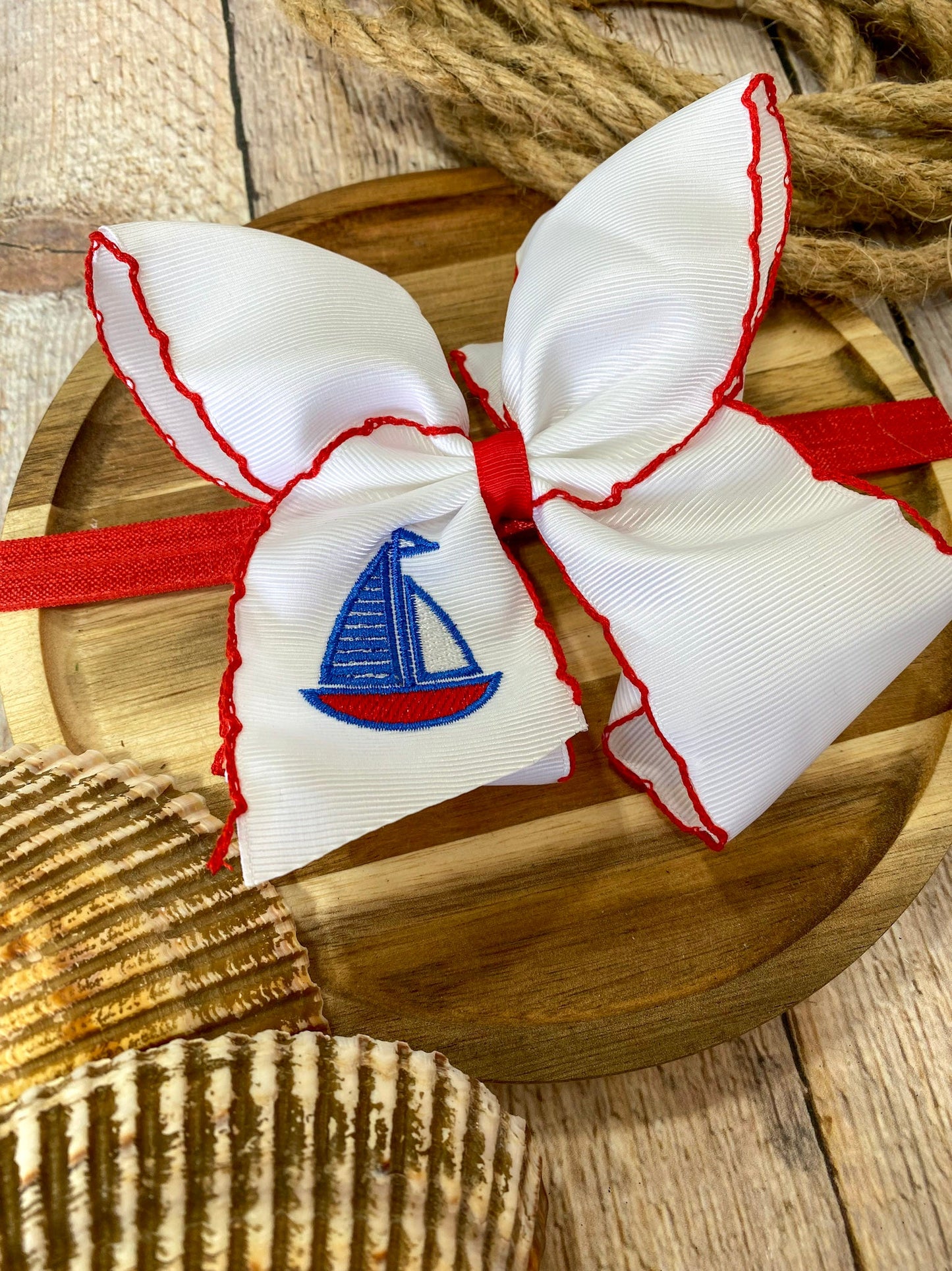white headband with red trim and embroidered sailboat on a wooden surface