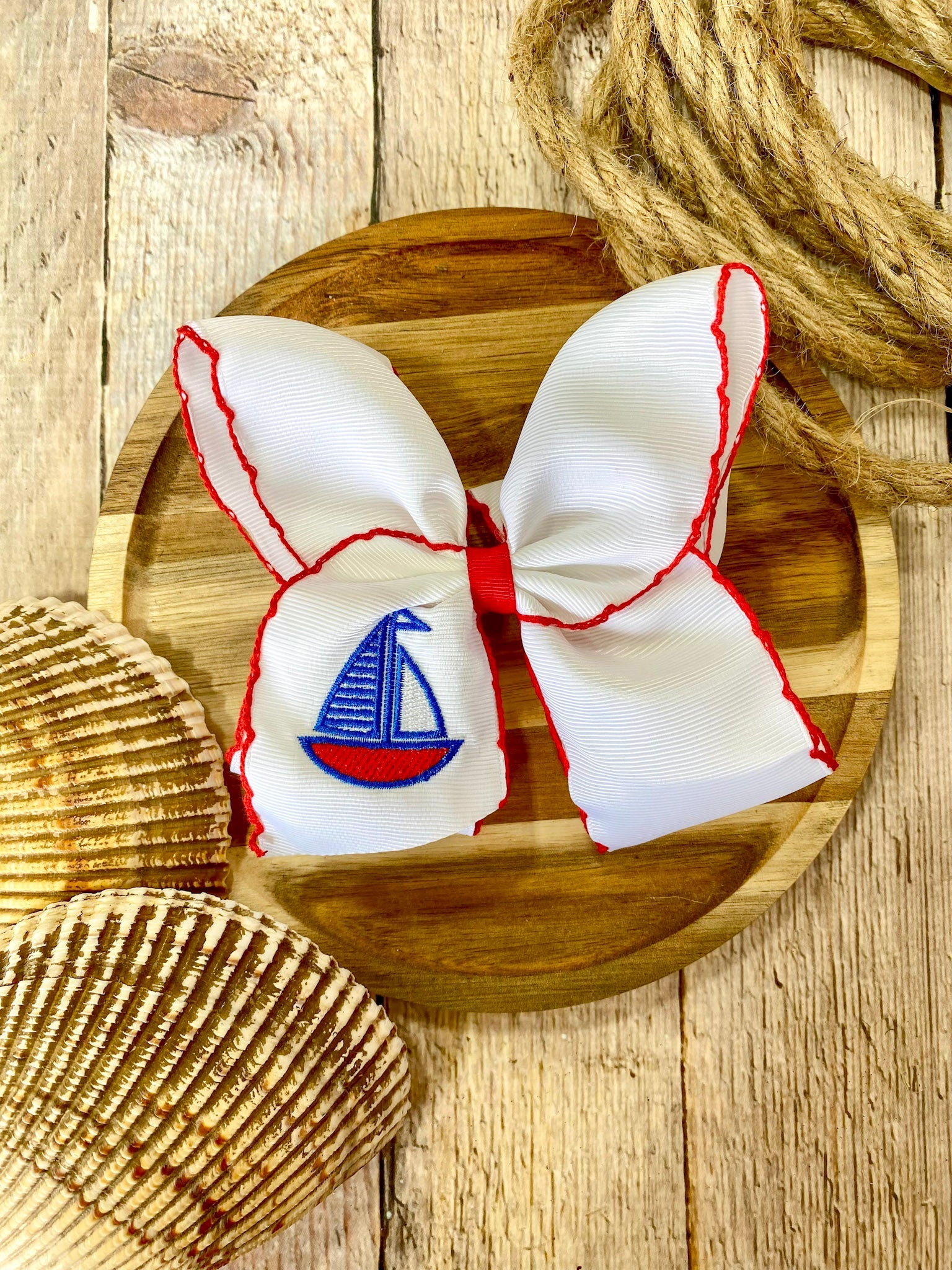white hairbow with red trim and embroidered sailboat on a wooden surface