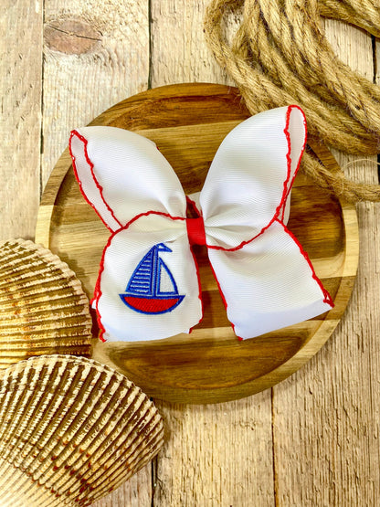 white hairbow with red trim and embroidered sailboat on a wooden surface