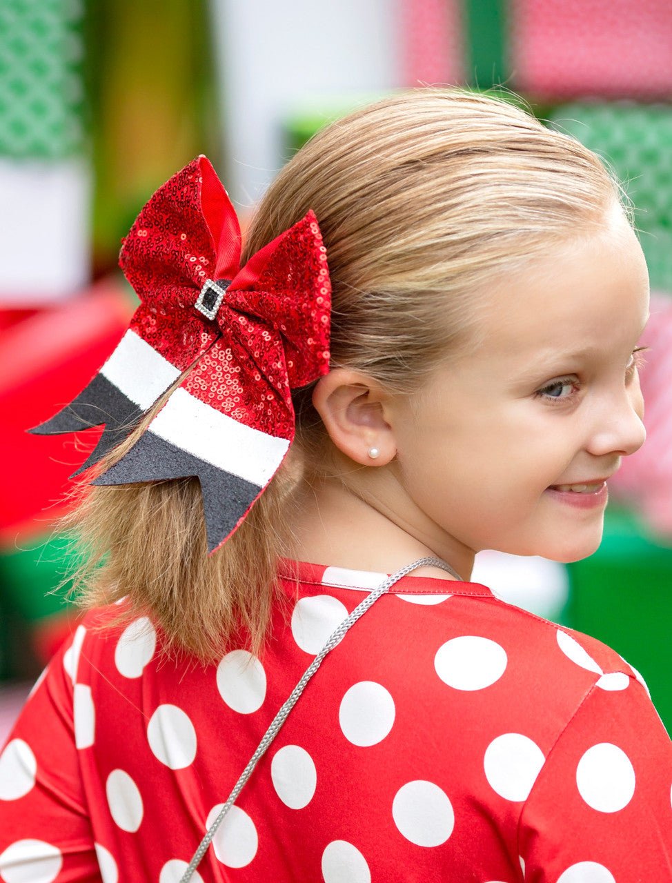 Child with a large red bow in their hair, wearing a red polka dot shirt.