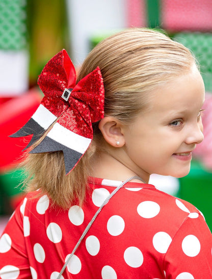 Child with a large red bow in their hair, wearing a red polka dot shirt.